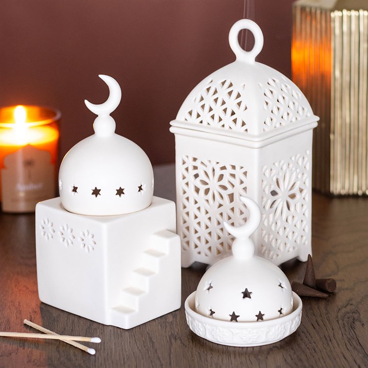 Set of white decorative lanterns on a wooden surface with a candle in the background.