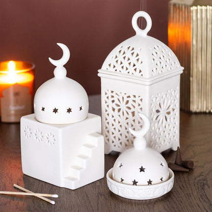 Set of white decorative lanterns on a wooden surface with a candle in the background.