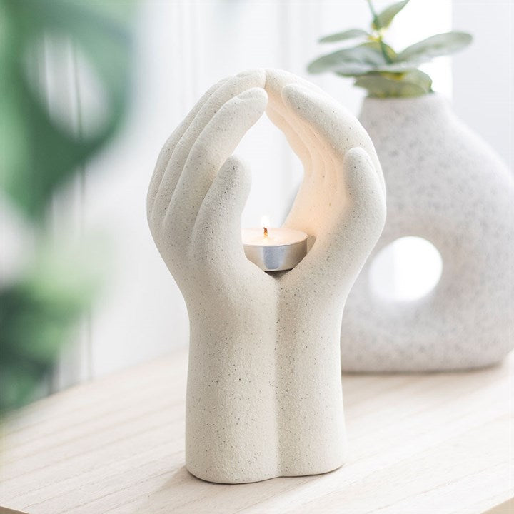 Ceramic candle holder shaped like a hand holding a candle, with a blurred plant in the background.