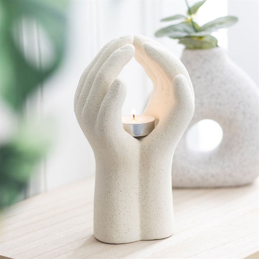 Ceramic candle holder shaped like a hand holding a candle, with a blurred plant in the background.