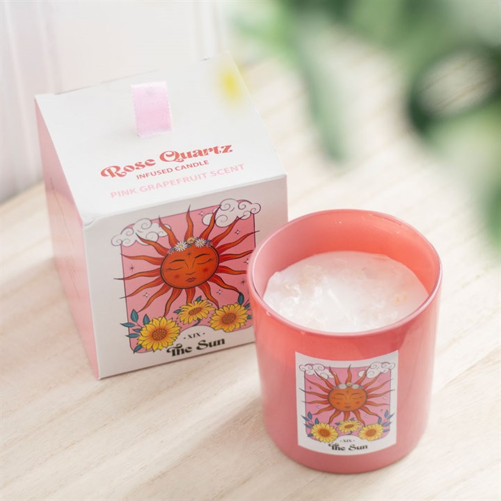 Pink candle with 'The Sun' design next to its packaging on a light surface.