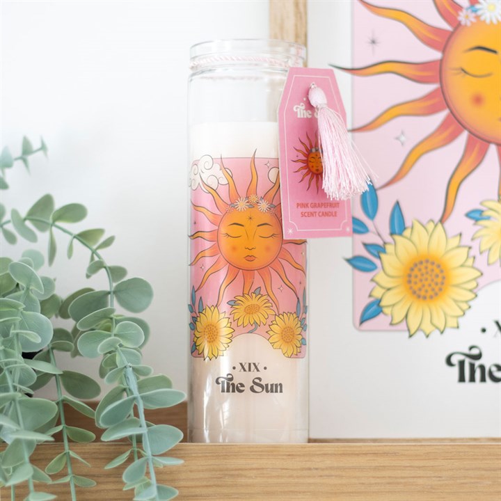Candle with sun design and decorative tag on a wooden surface with plants in the background
