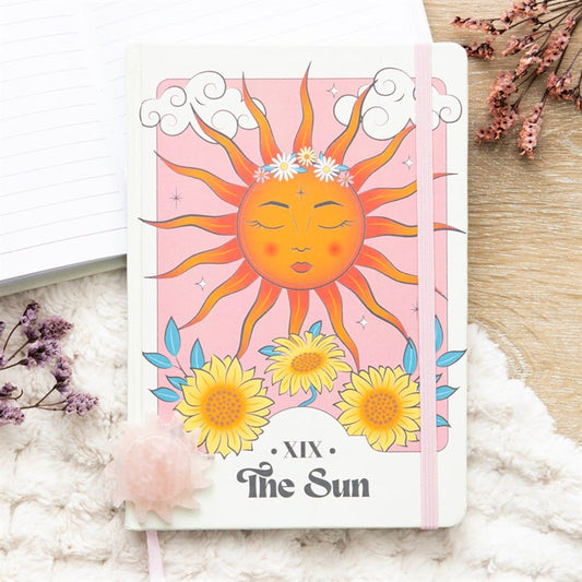 Notebook with a sun design and 'The Sun' text on a soft surface with flowers.