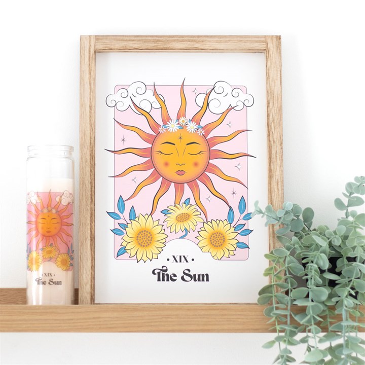 Framed artwork of a sun with flowers on a white wall with a plant and candle in the background.