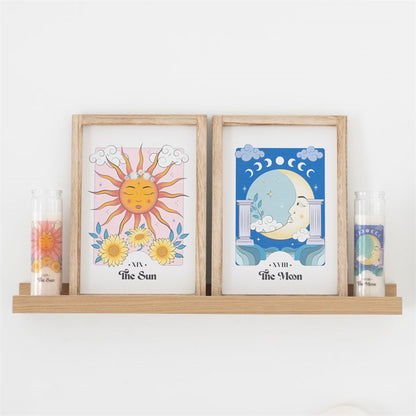 Two framed illustrations of the sun and moon on a shelf with candles.