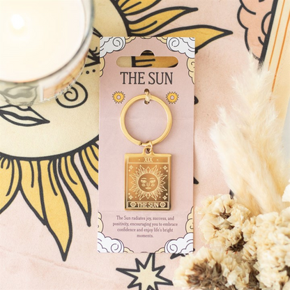 Gold keychain with 'The Sun' design on packaging, surrounded by decorative elements.