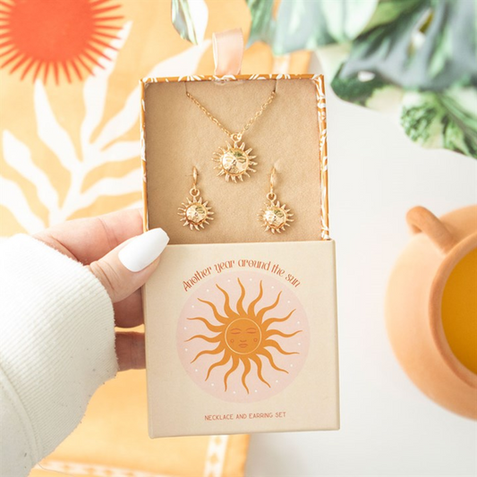 Gold sun-themed necklace and earrings set in a decorative box with a sun design, held by a hand.