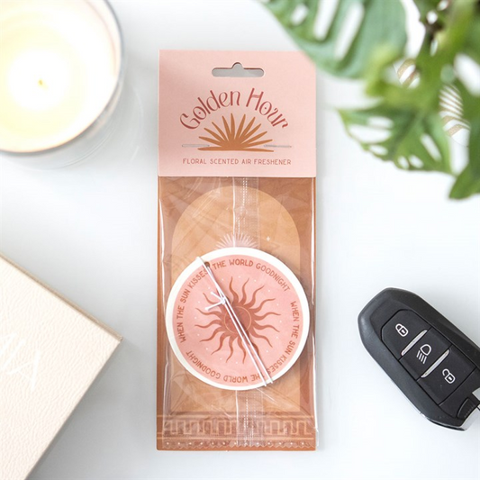 Packaged Golden Hour floral scented air freshener on a white surface with a car key and plant in the background.