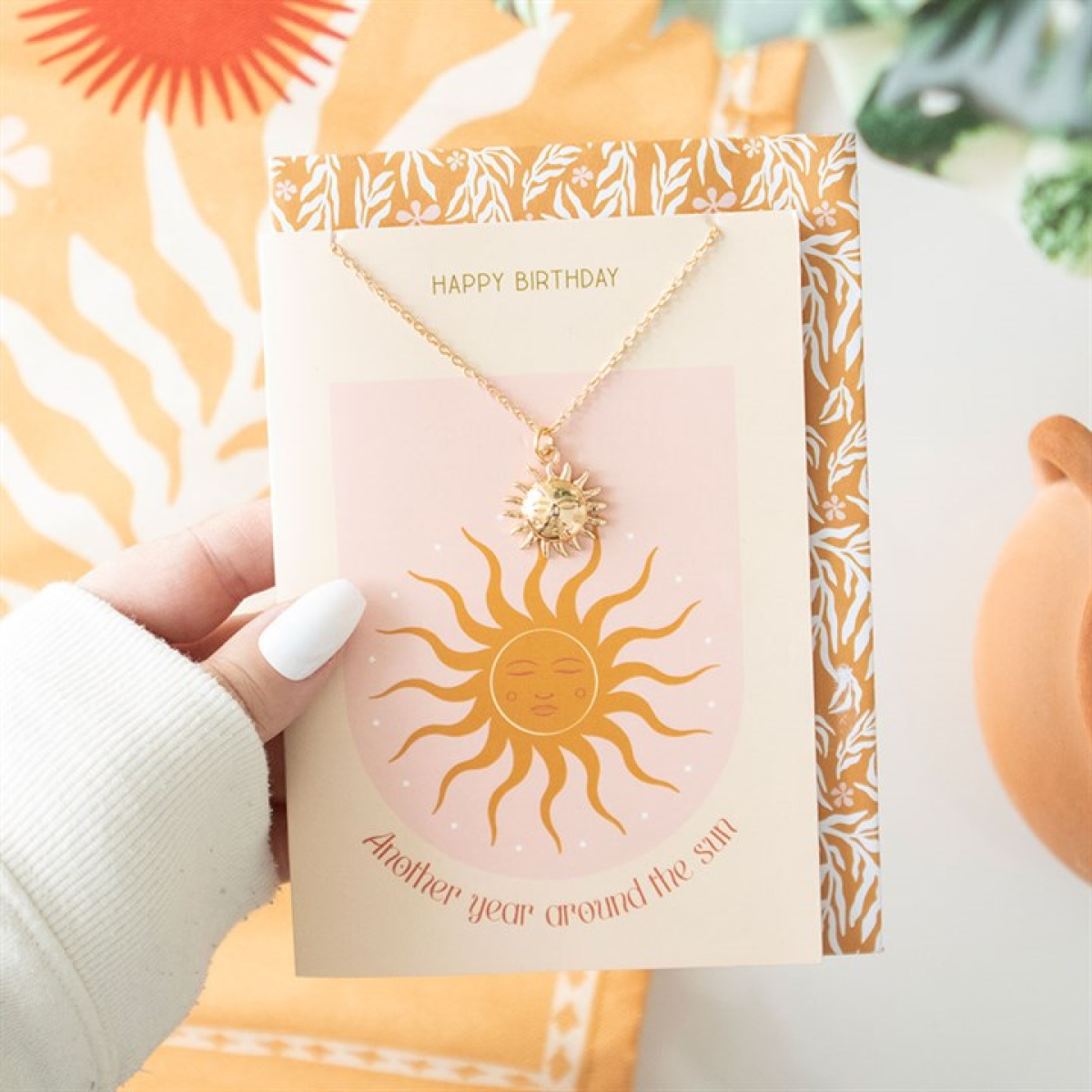 Necklace with sun design on a 'Happy Birthday' card held by a hand.