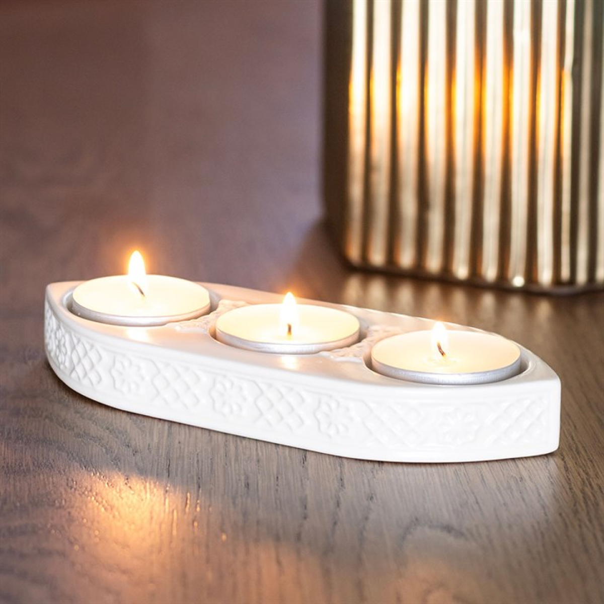 White ceramic holder with three lit candles on a wooden surface