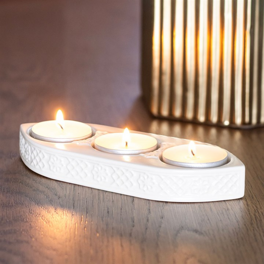 White ceramic holder with three lit candles on a wooden surface