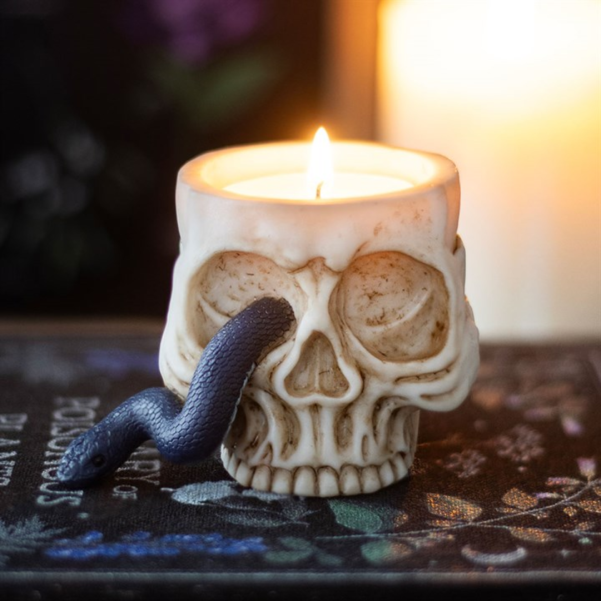 Skull-shaped candle with a snake on a dark surface with a blurred background