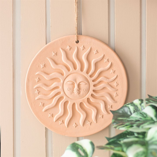 Decorative sun wall hanging on a neutral background with a plant