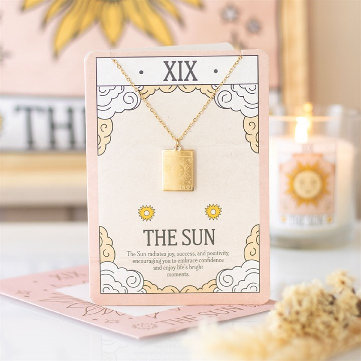 Necklace with a gold pendant on a greeting card with 'The Sun' theme, placed on a surface with a blurred background.