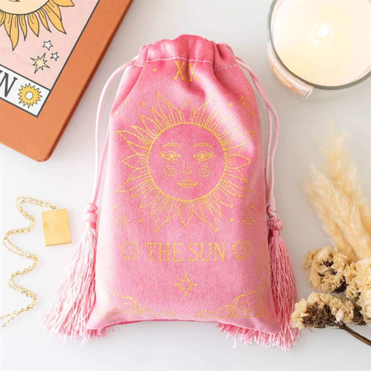 Pink drawstring bag with sun design and 'The Sun' text on a white surface with tarot cards and candles.