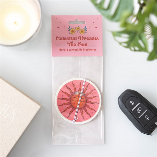Pink celestial-themed air freshener in packaging on a white surface with a candle and car key visible.